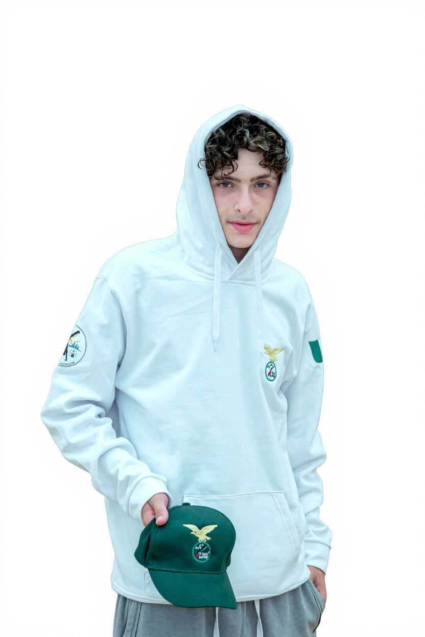 Ragazzo con felpa bianca con cappuccio ricamata, tiene in mano il cappellino verde