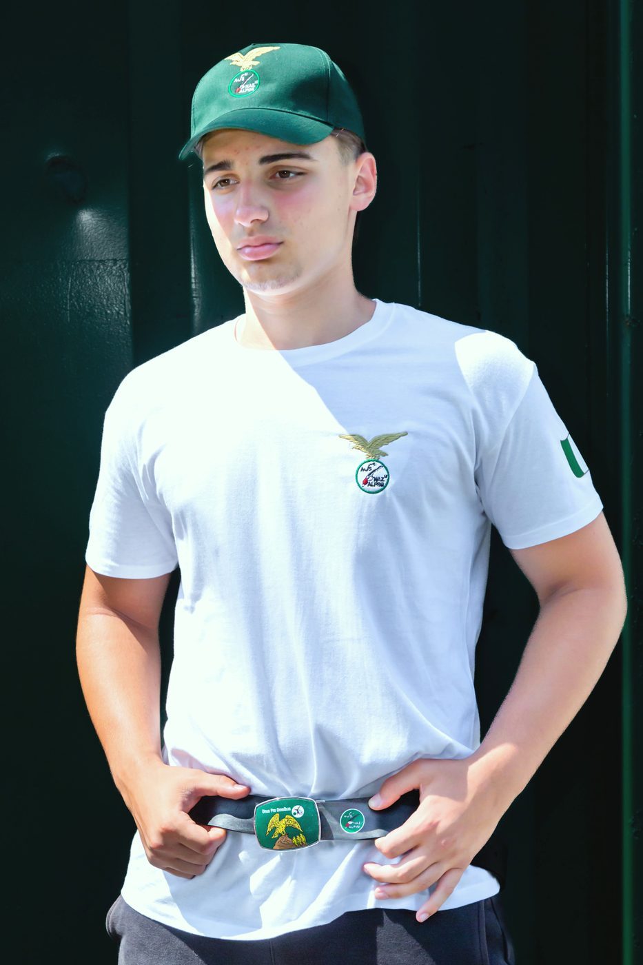 Ragazzo con cintura con fibbia decorata ad aquila, maglietta bianca e cappellino verde