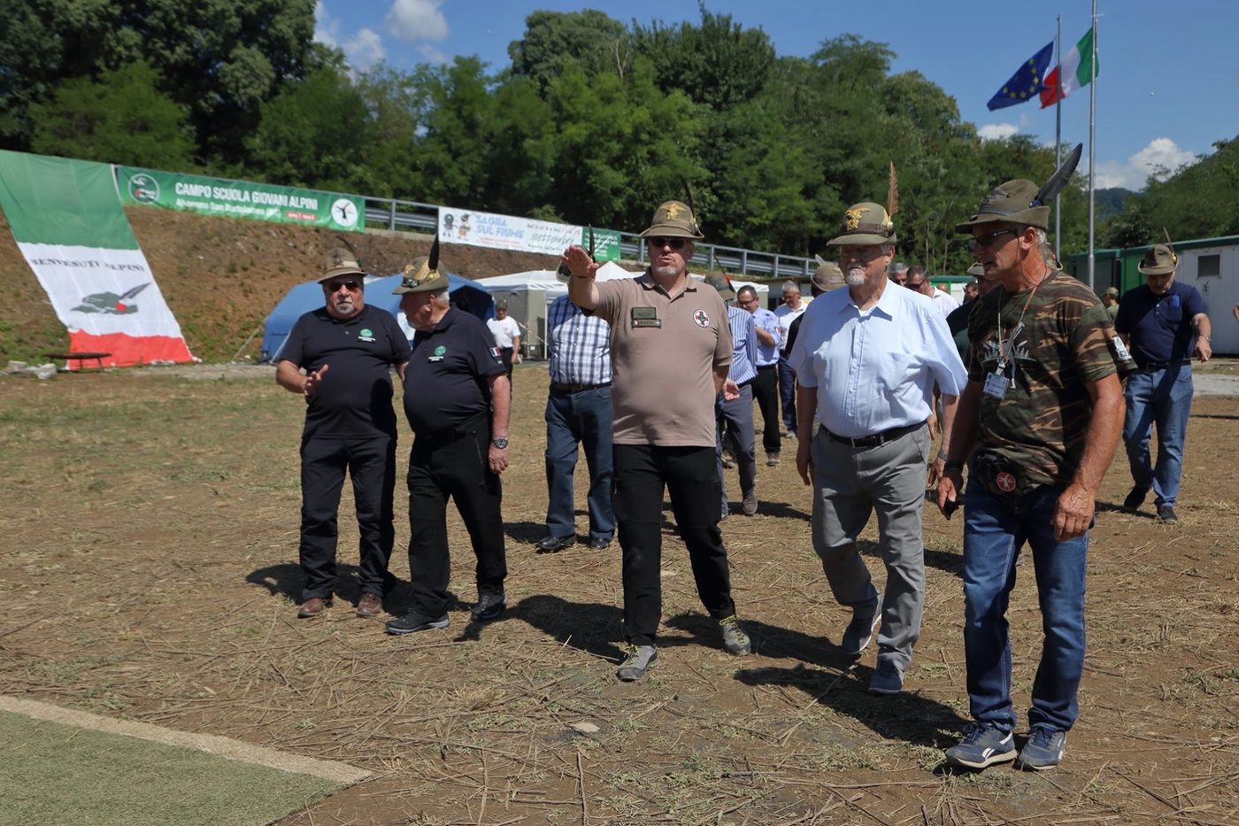 Delegazione Alpini in visita al campo, davanti al banner Sagra sul Fiume