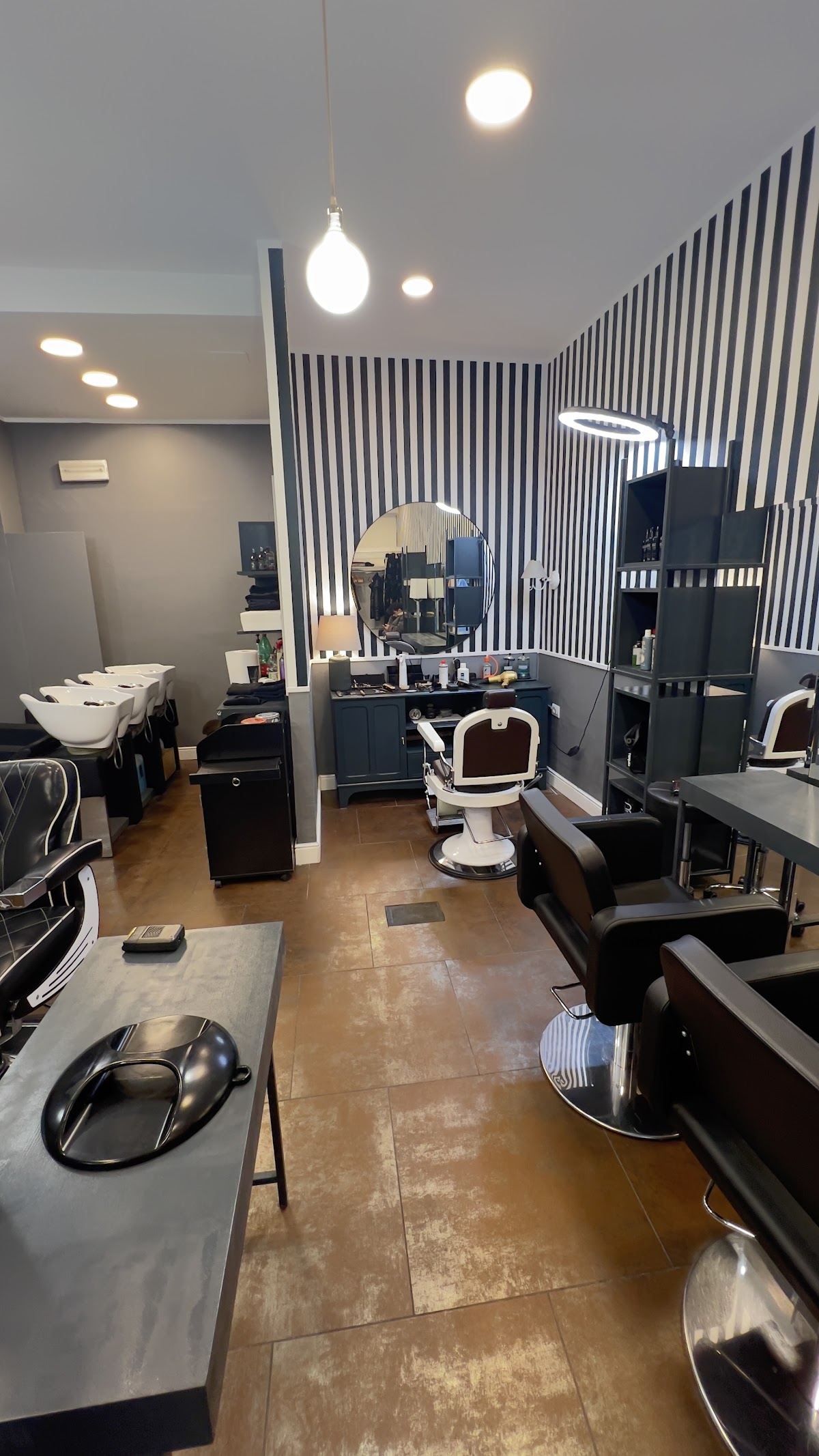 Sala del barbershop con parete a righe bianco e nero e poltrone in pelle nera